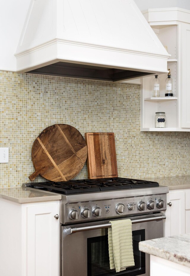 kitchen featuring premium range hood, white cabinets, high end stove, light stone counters, and tasteful backsplash