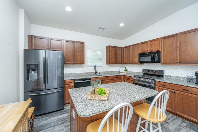 kitchen featuring a kitchen breakfast bar, visible vents, a sink, black appliances, and dark wood-type flooring
