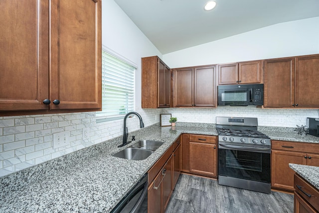 kitchen with decorative backsplash, light stone countertops, dark wood finished floors, a sink, and black appliances