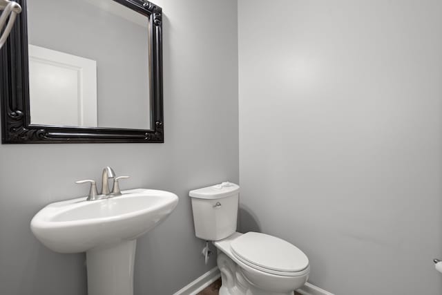 half bathroom featuring toilet, baseboards, and a sink