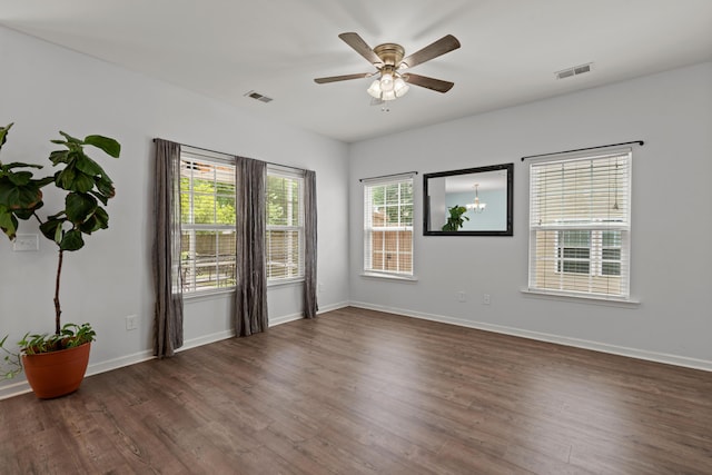 unfurnished room featuring baseboards, a ceiling fan, visible vents, and dark wood finished floors