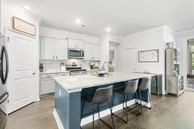 kitchen featuring a kitchen breakfast bar, stainless steel appliances, white cabinetry, and a kitchen island with sink