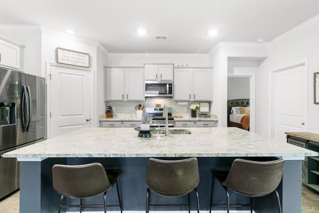 kitchen with sink, tasteful backsplash, crown molding, an island with sink, and appliances with stainless steel finishes