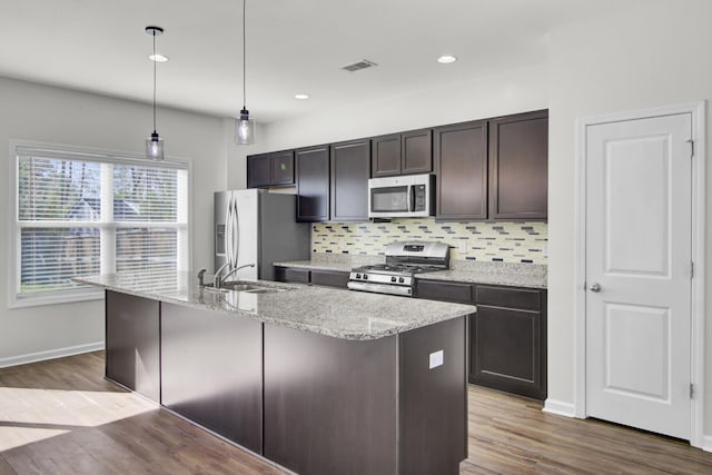 kitchen with pendant lighting, dark brown cabinetry, stainless steel appliances, hardwood / wood-style flooring, and a center island with sink