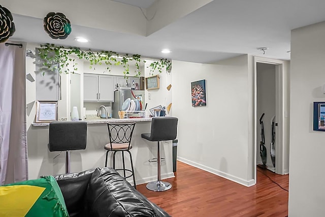 kitchen featuring wood finished floors, freestanding refrigerator, a sink, light countertops, and a kitchen bar