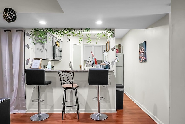 kitchen with a breakfast bar area, wood finished floors, baseboards, a peninsula, and stainless steel appliances