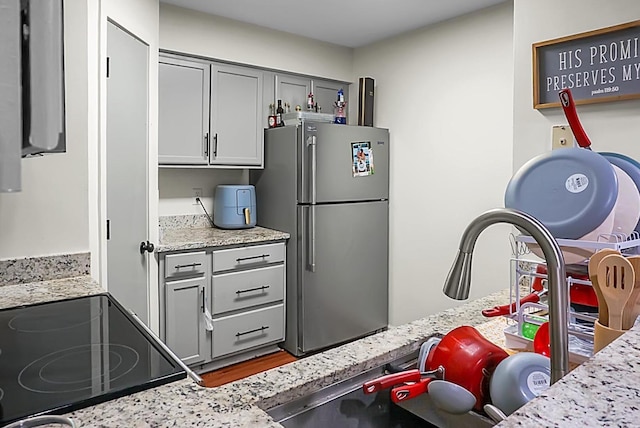 kitchen with electric range, light stone countertops, gray cabinets, and freestanding refrigerator