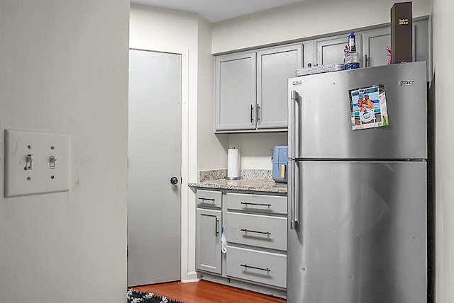 kitchen featuring light stone countertops, wood finished floors, gray cabinets, and freestanding refrigerator