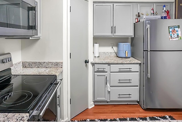 kitchen with light stone counters, appliances with stainless steel finishes, gray cabinetry, and light wood finished floors