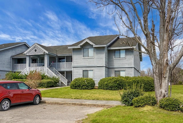 multi unit property with stairs, covered porch, roof with shingles, and a front lawn