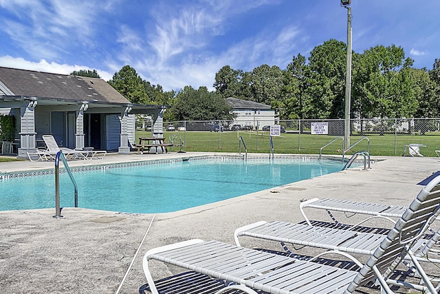 community pool with a patio, a lawn, and fence