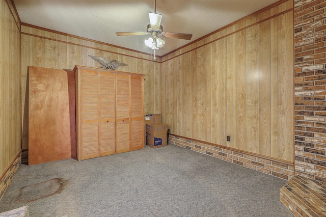 unfurnished bedroom with a ceiling fan, a closet, wooden walls, carpet, and crown molding