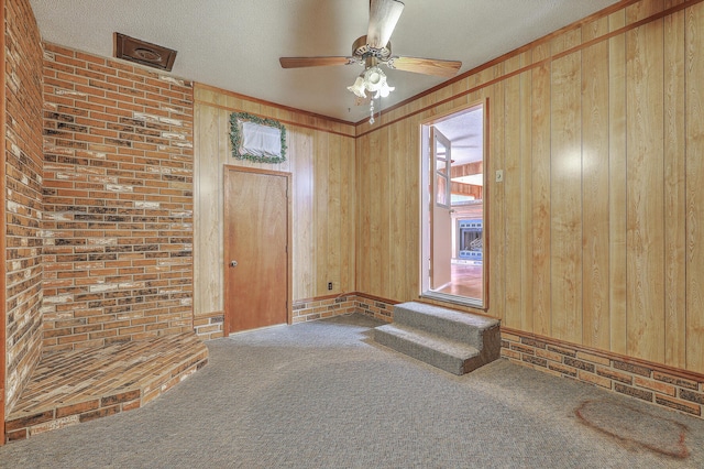 carpeted empty room with wooden walls, a textured ceiling, and a ceiling fan