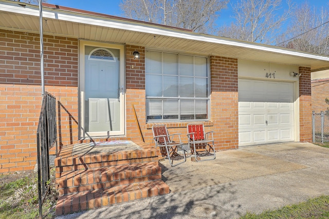 entrance to property featuring driveway, brick siding, and an attached garage