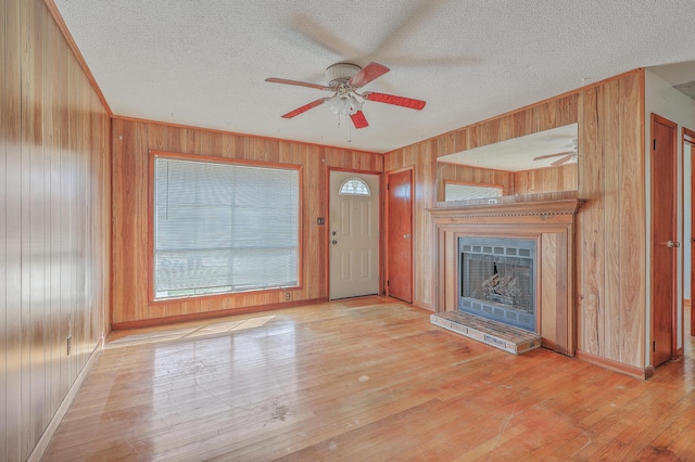 unfurnished living room with hardwood / wood-style floors, a textured ceiling, a fireplace with raised hearth, and wood walls