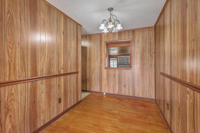 unfurnished dining area featuring wooden walls, a notable chandelier, light wood finished floors, and a textured ceiling