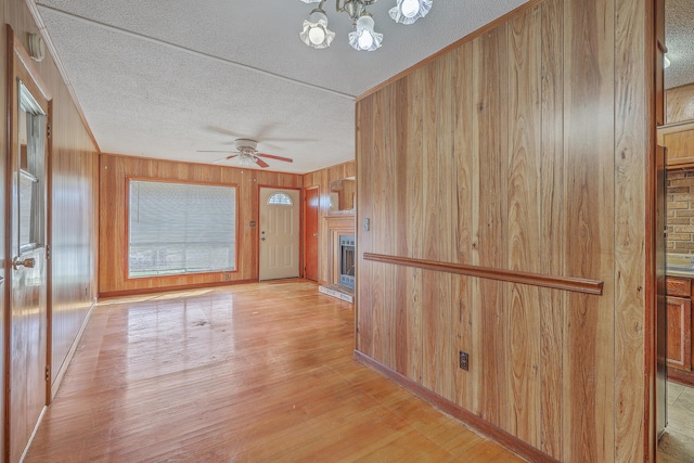 corridor featuring light wood finished floors, a notable chandelier, wood walls, and a textured ceiling