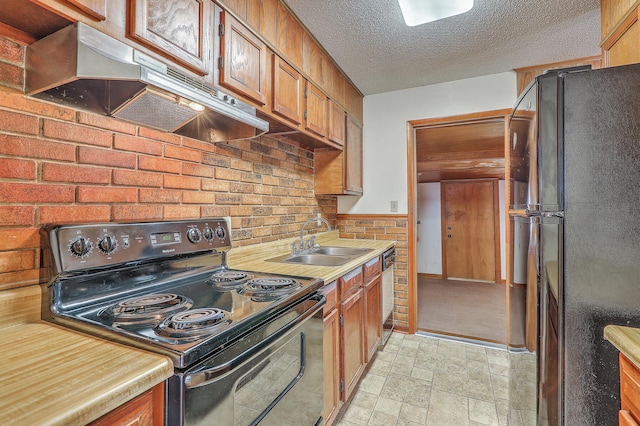 kitchen featuring a sink, black appliances, stone finish flooring, under cabinet range hood, and a textured ceiling