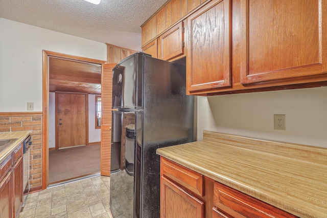 kitchen featuring stone finish flooring, a wainscoted wall, light countertops, freestanding refrigerator, and a textured ceiling