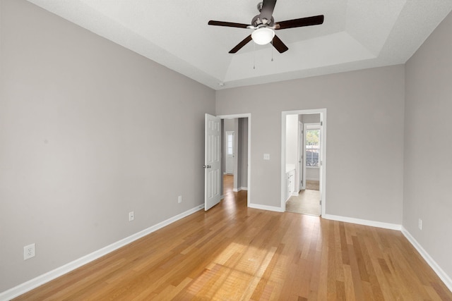 unfurnished bedroom with ceiling fan, light hardwood / wood-style floors, and a tray ceiling