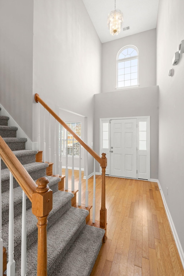 foyer with wood-type flooring, a towering ceiling, and an inviting chandelier