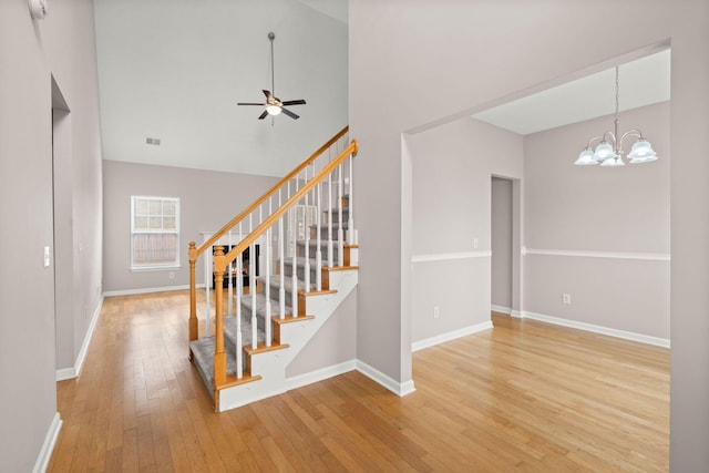 stairway featuring hardwood / wood-style floors, ceiling fan with notable chandelier, and high vaulted ceiling