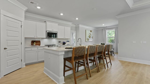212 Bilge Rd, Ridgeville, SC 29472 - kitchen featuring stainless steel microwave, ornamental molding, a center island with sink, light wood-style floors, and decorative backsplash
