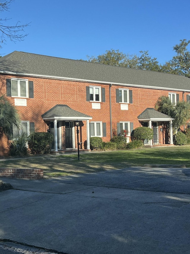 view of front of property with a shingled roof, a front lawn, and brick siding