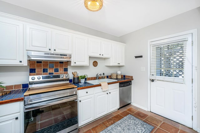 kitchen featuring tile counters, appliances with stainless steel finishes, white cabinetry, a sink, and under cabinet range hood