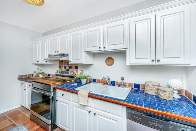 kitchen featuring tile countertops, appliances with stainless steel finishes, under cabinet range hood, white cabinetry, and a sink