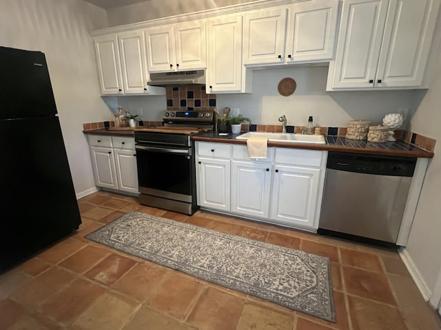 kitchen with stainless steel appliances, tile counters, white cabinetry, a sink, and under cabinet range hood