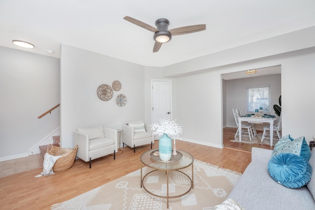 living area with light wood finished floors, ceiling fan, stairs, and baseboards