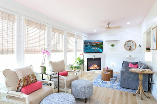 living area with a wall unit AC, lofted ceiling, a glass covered fireplace, ceiling fan, and wood finished floors