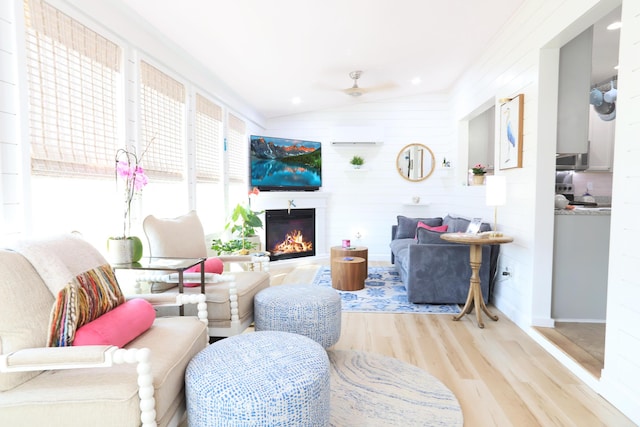 living room featuring lofted ceiling, a warm lit fireplace, ceiling fan, and wood finished floors