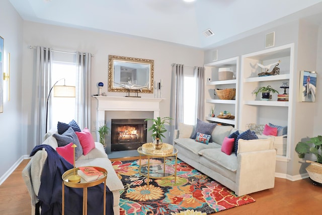 living room with a fireplace with flush hearth, visible vents, baseboards, and wood finished floors