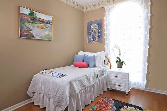 bedroom with multiple windows, baseboards, and wood finished floors