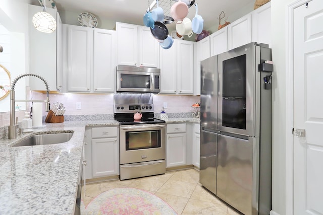 kitchen featuring light stone counters, a sink, white cabinetry, appliances with stainless steel finishes, and decorative backsplash