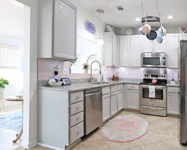 kitchen with tasteful backsplash, visible vents, appliances with stainless steel finishes, light stone countertops, and a sink