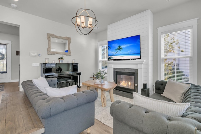 living room featuring a notable chandelier, a glass covered fireplace, a healthy amount of sunlight, and wood finished floors