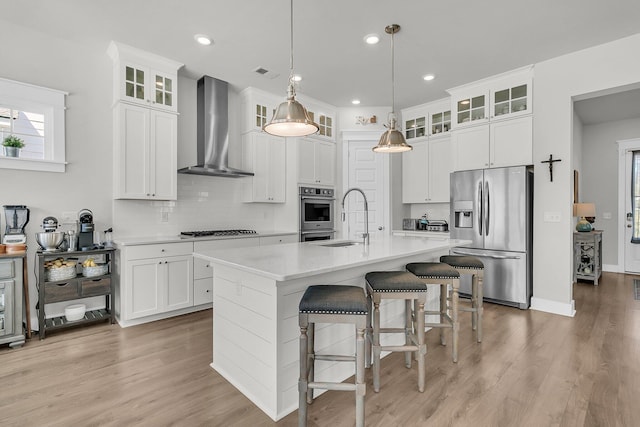 kitchen featuring visible vents, wall chimney range hood, stainless steel fridge with ice dispenser, light countertops, and a sink