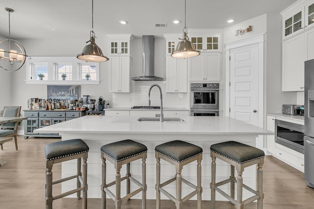 kitchen featuring visible vents, backsplash, wood finished floors, wall chimney exhaust hood, and light countertops