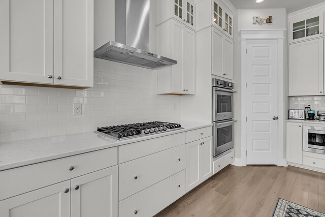 kitchen with white cabinetry, wall chimney range hood, light wood-style floors, and appliances with stainless steel finishes