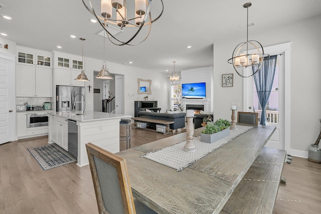 dining space with a chandelier, recessed lighting, a warm lit fireplace, and light wood-style floors