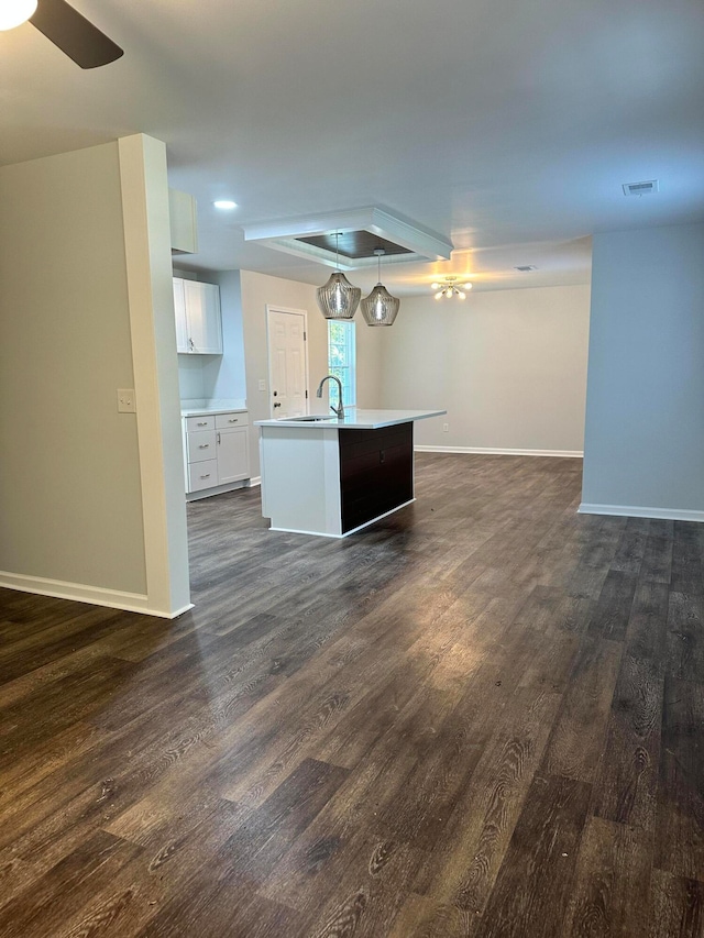 interior space with a kitchen island with sink, dark hardwood / wood-style flooring, sink, hanging light fixtures, and white cabinets