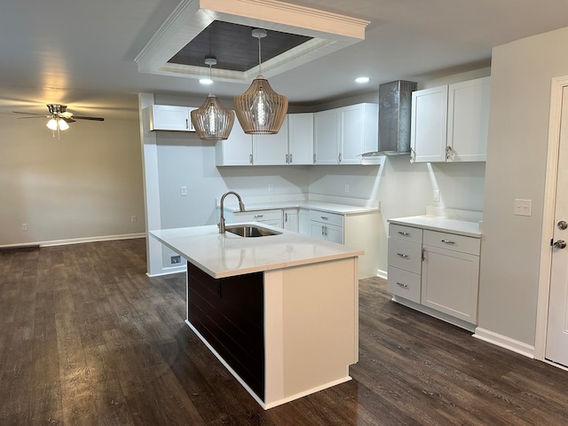 kitchen with white cabinets, wall chimney exhaust hood, a raised ceiling, and sink