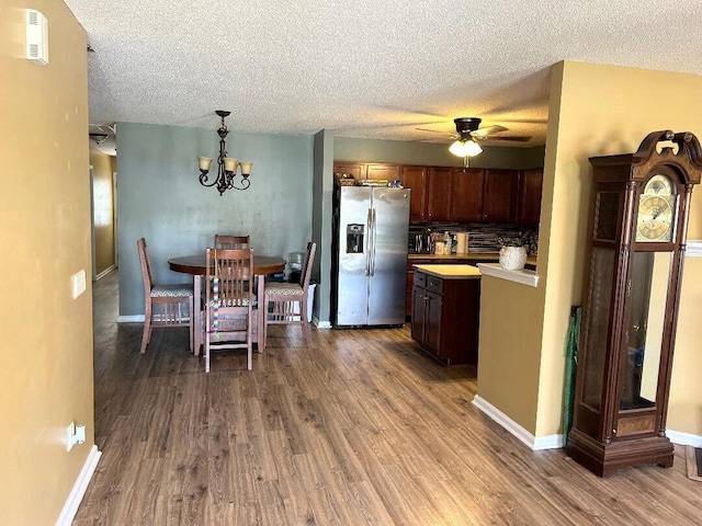 kitchen featuring ceiling fan with notable chandelier, stainless steel fridge with ice dispenser, pendant lighting, and dark wood-type flooring