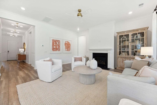 living room featuring a fireplace with flush hearth, crown molding, baseboards, and wood finished floors