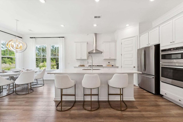 kitchen featuring wall chimney exhaust hood, visible vents, appliances with stainless steel finishes, and a kitchen breakfast bar