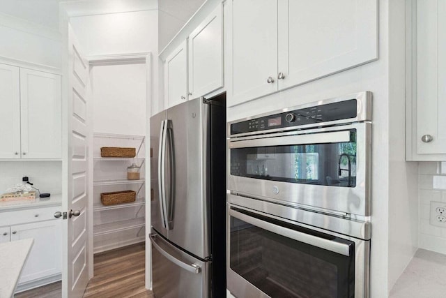 kitchen with tasteful backsplash, appliances with stainless steel finishes, wood finished floors, light countertops, and white cabinetry