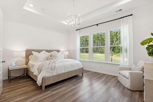 bedroom featuring an inviting chandelier, baseboards, a tray ceiling, and wood finished floors